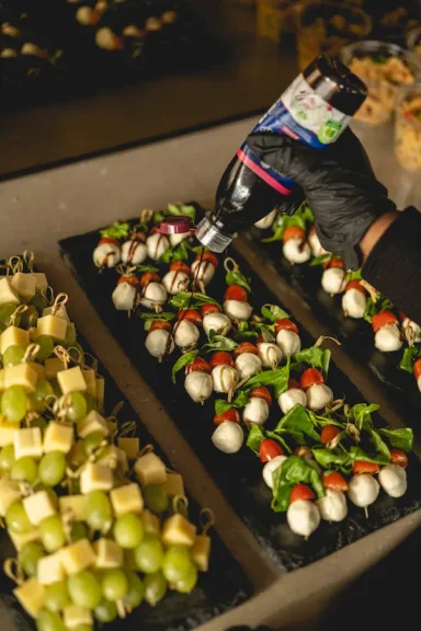 Tomate-Mozzarella- und Weintraiben-Käse-Spieße und eine Hand, die Balsamico darüber verteilt