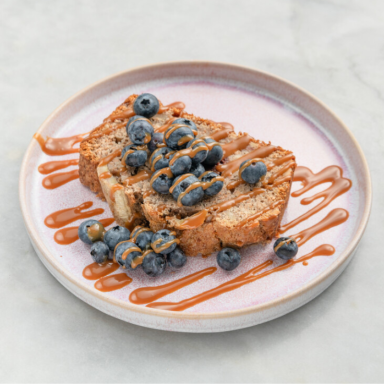 Eine Scheibe hausgemachtes Banana Bread mit Blaubeeren und Sirup